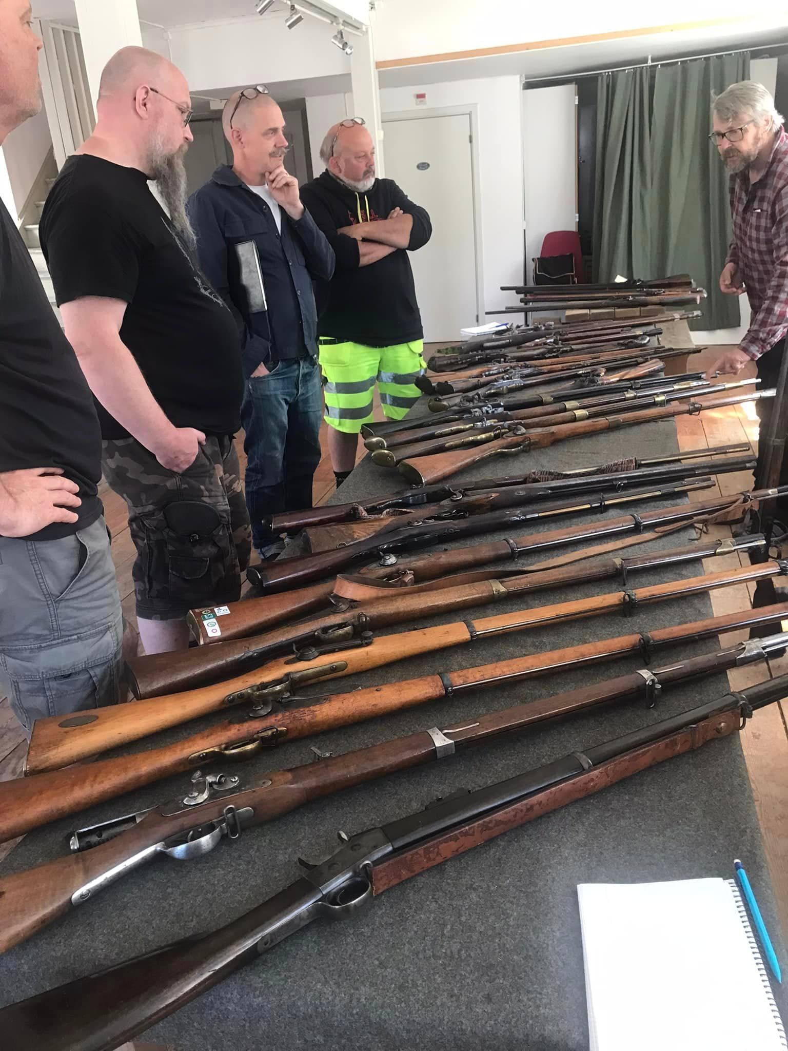 Kursdeltagare studerar antika långvapen på ett bord inomhus.
