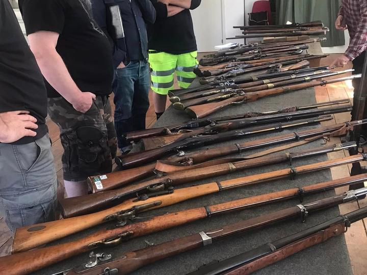 Kursdeltagare studerar antika långvapen på ett bord inomhus.