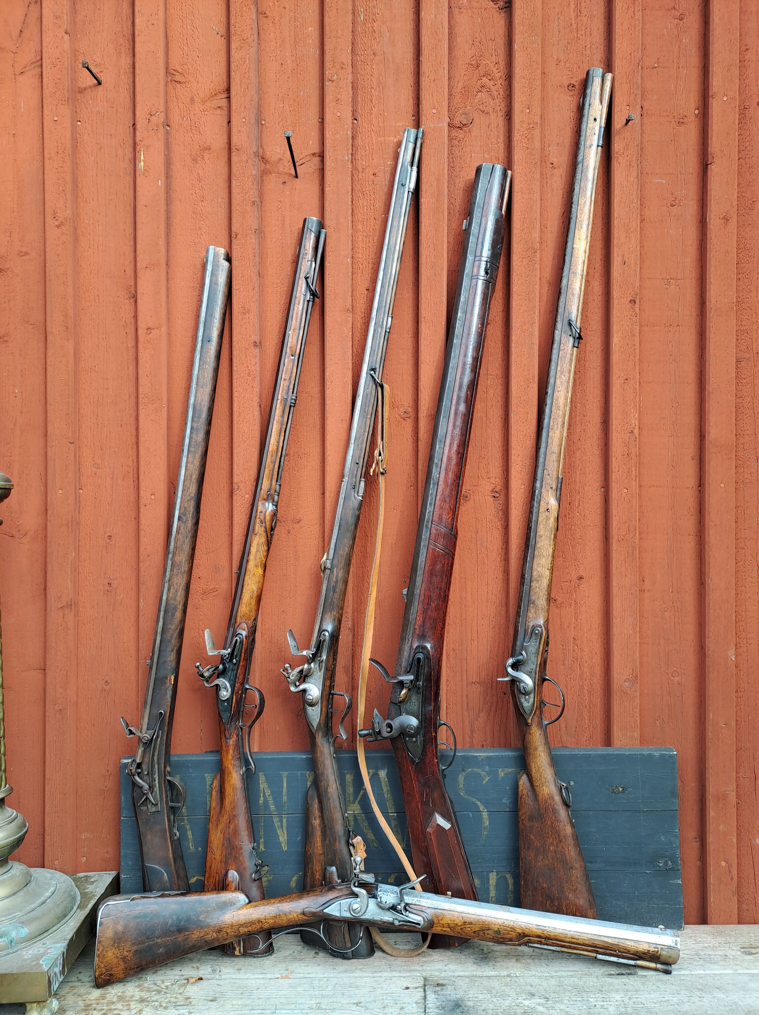 Samling av antika långvapen uppställda mot en röd trävägg.