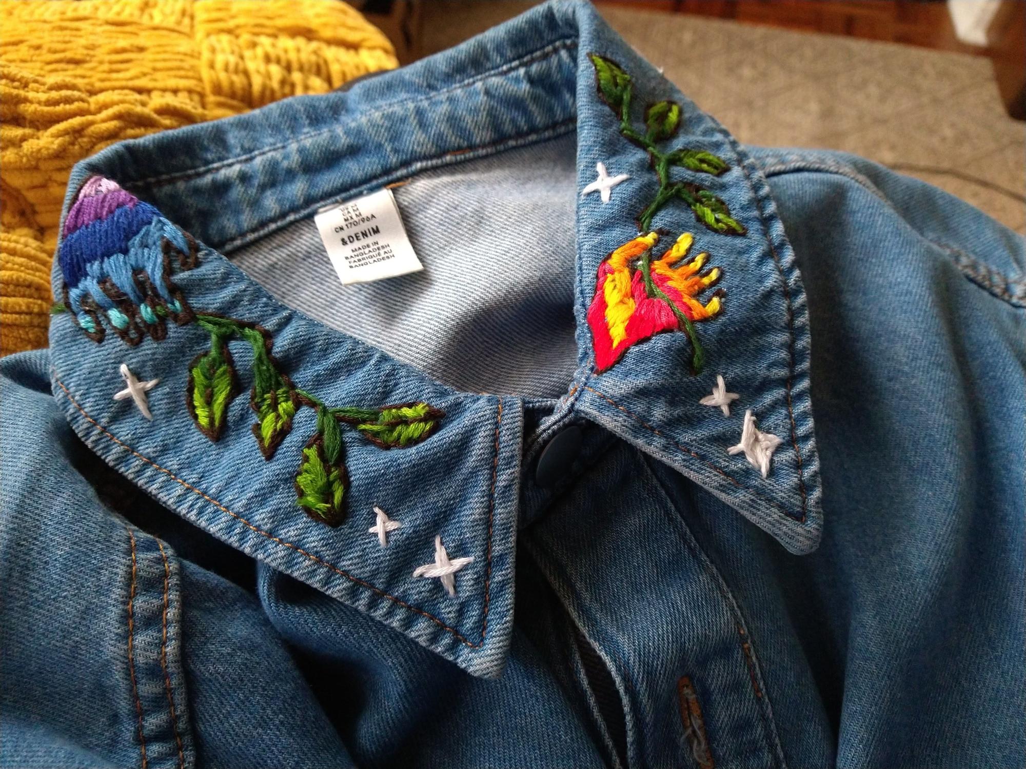 A jean romper collar embroidered with colourful hands, green leaves and stars.
