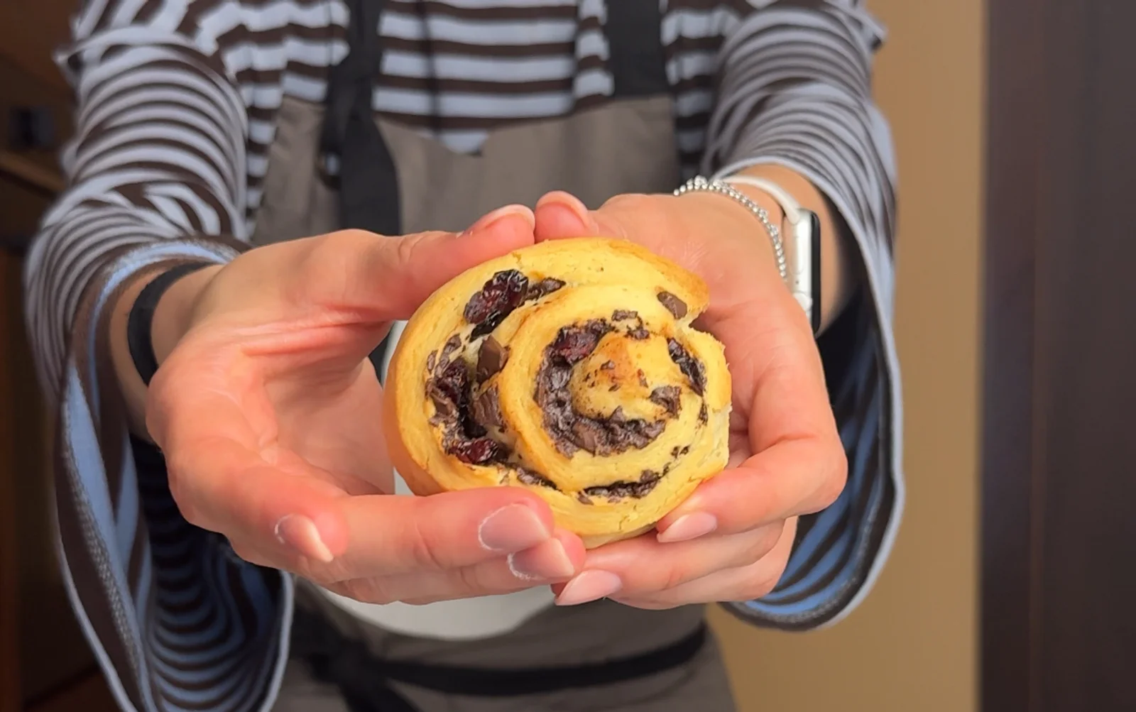 Golden-brown ricotta chocolate cranberry rolls with dark chocolate chunks and fruit swirls on white parchment paper.