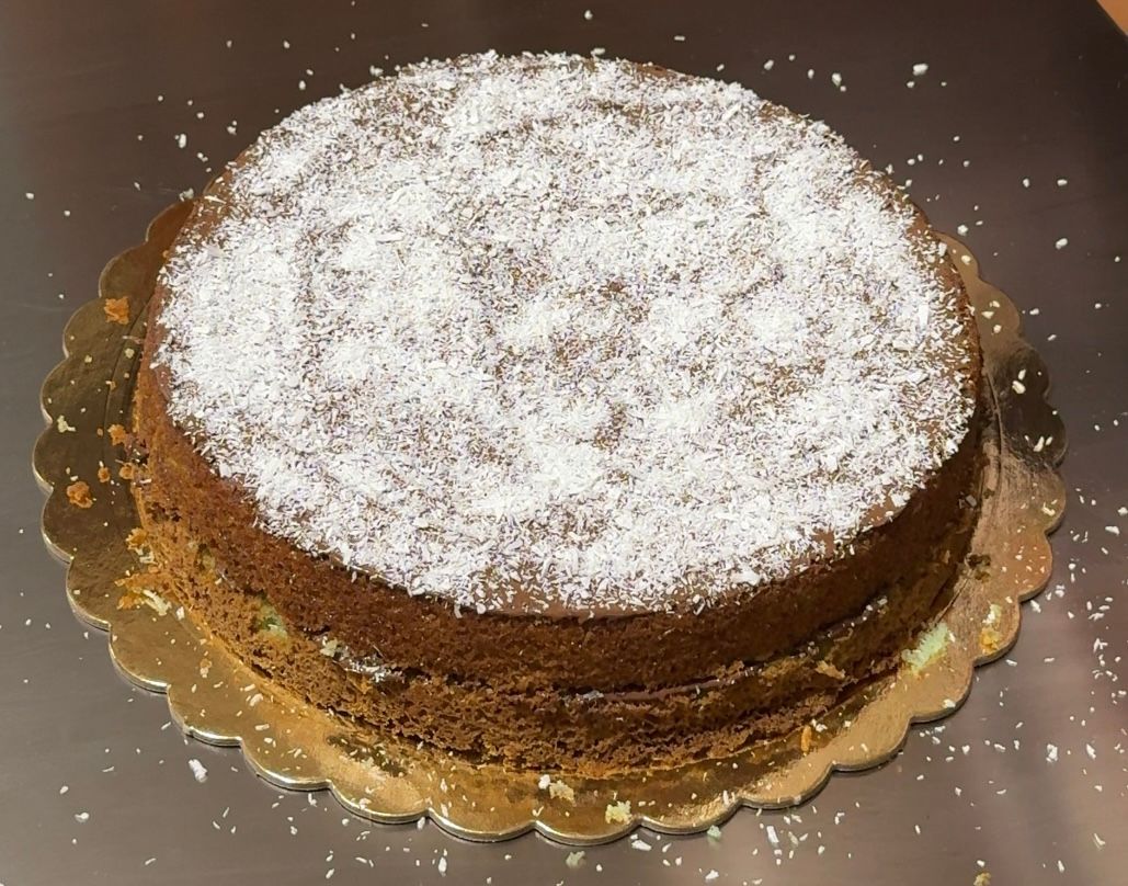 Hand sprinkling desiccated coconut over a coconut Nutella mint cake on a gold board, viewed from above.