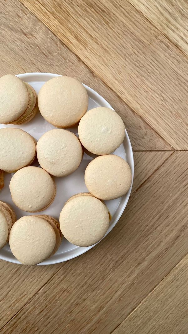 White chocolate salted caramel macarons with smooth almond shells arranged on a white plate over a wooden table.