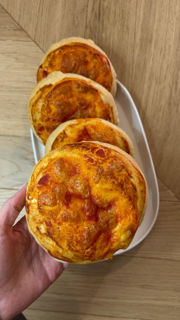 Hand holding golden bakery style mini pizzas recipe with melted cheese and tomato sauce, stacked on a white plate
