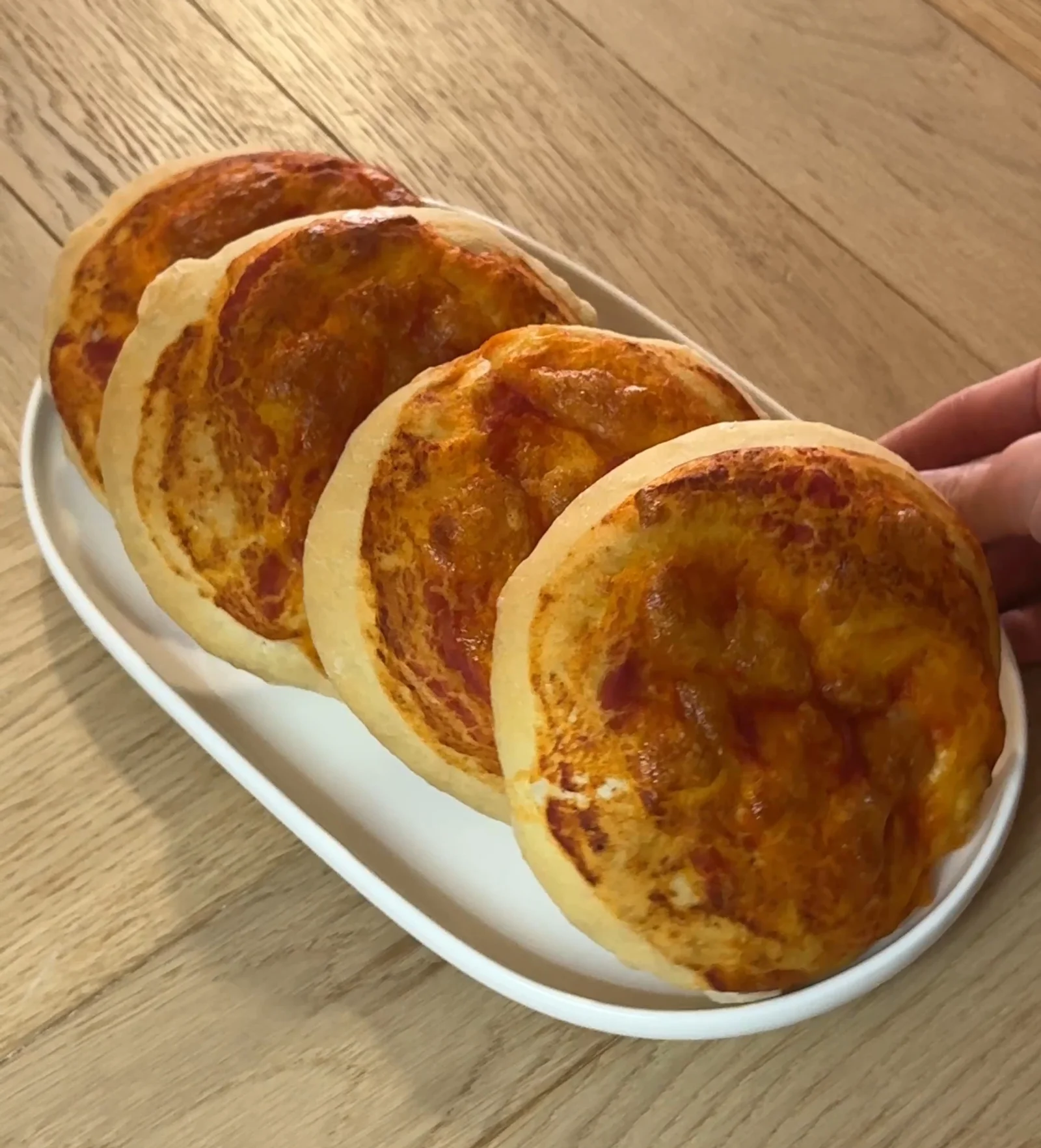Hand holding golden bakery style mini pizzas recipe with melted cheese and tomato sauce, stacked on a white plate
