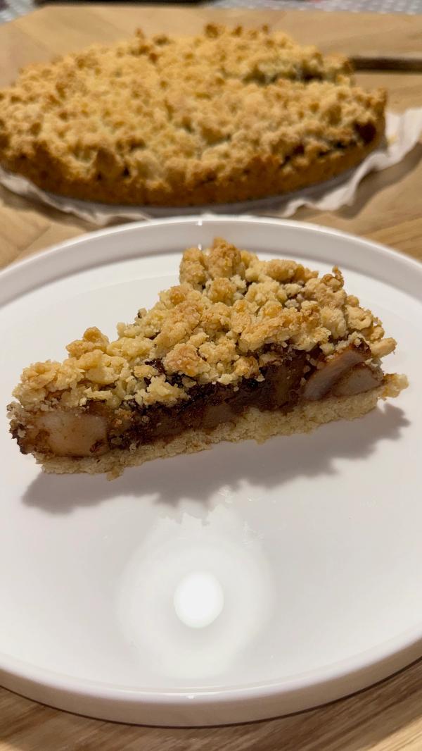 Slice of pear chocolate crumble cake with golden oat topping, pear chunks and dark chocolate filling on a white plate.