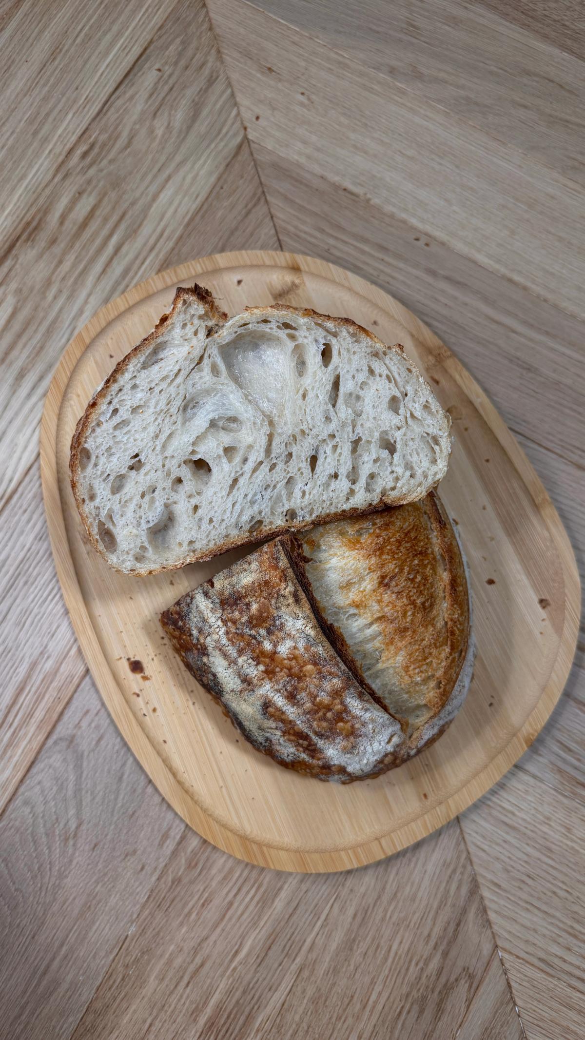 Sliced sourdough bread recipe beginner loaf on wooden board, showing open crumb and golden crispy crust