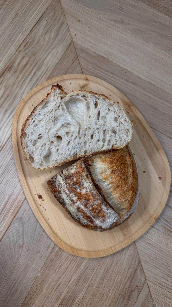 Sliced sourdough bread recipe beginner loaf on wooden board, showing open crumb and golden crispy crust