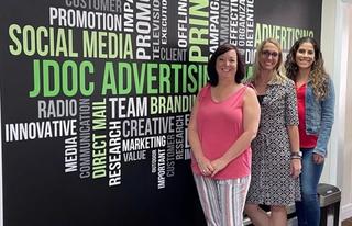 Jill, Yaslin, and client standing in front of wall filled with advertising words