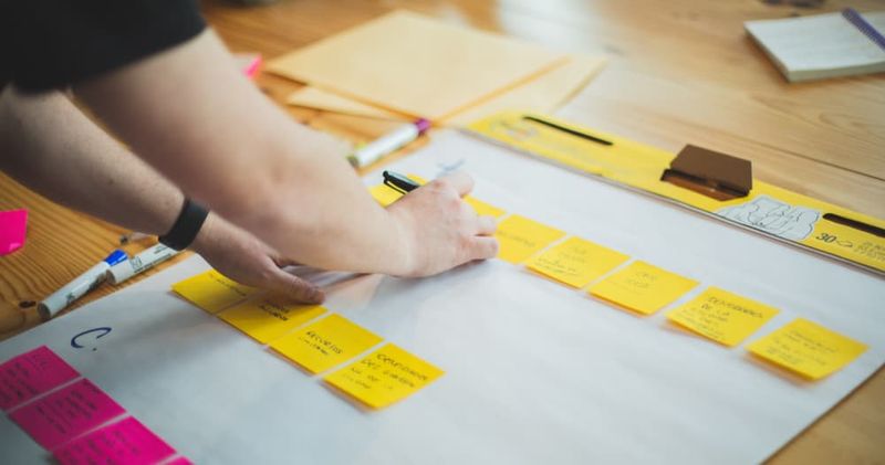 Person placing yellow and pink sticky notes on large notepad