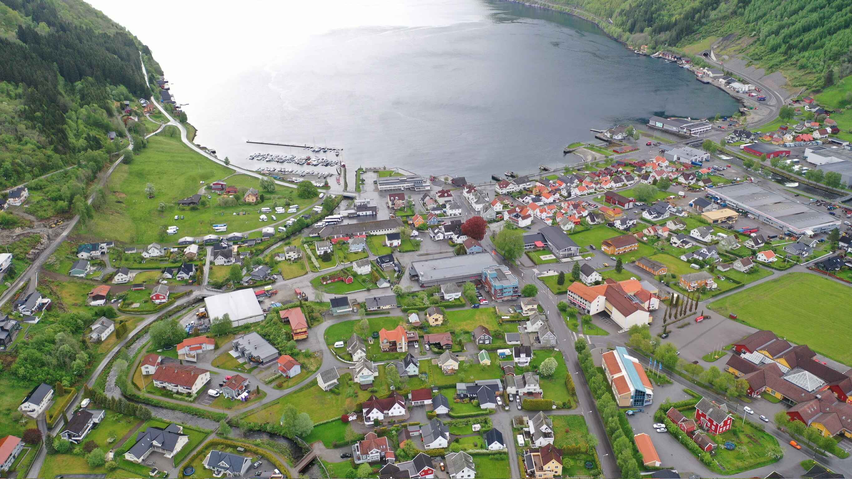 Aerial view of Vikøyri with view of a calm Sognefjord with boats docked at a pier, surrounded by greenery and hills.