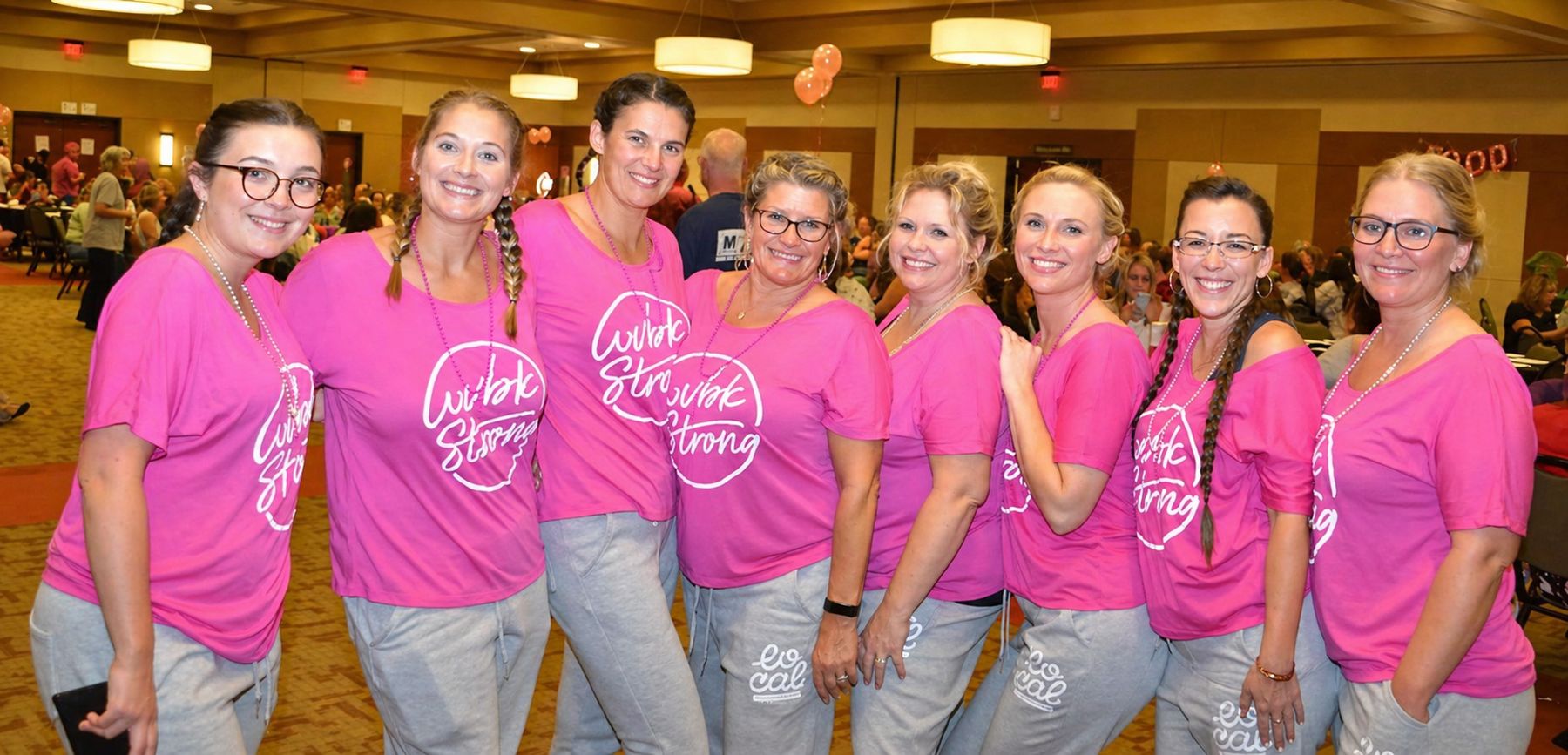 A group of women in matching custom pink shirts pose together at a company event.”