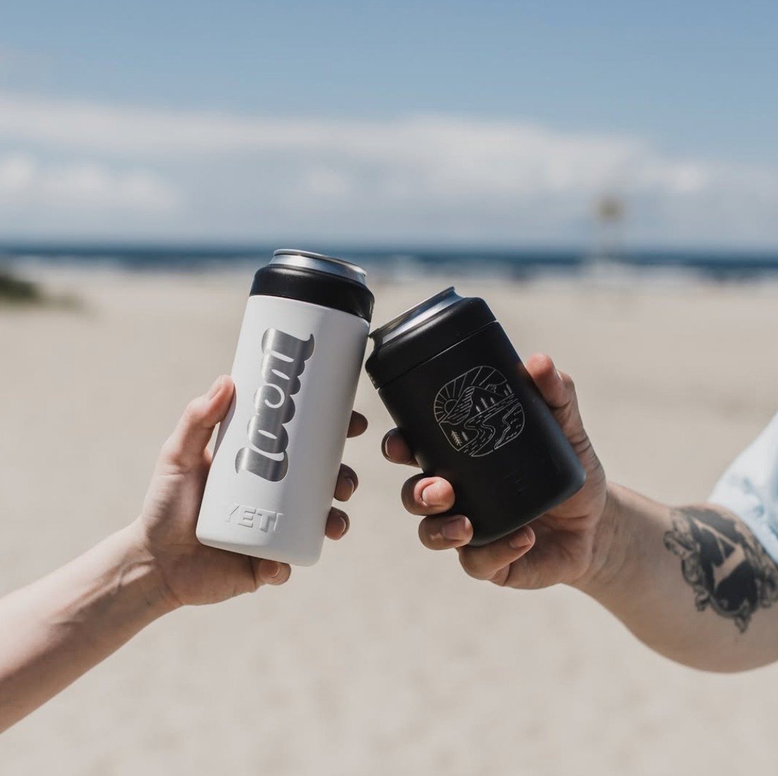 Two hands holding branded drink coolers against a beach backdrop.