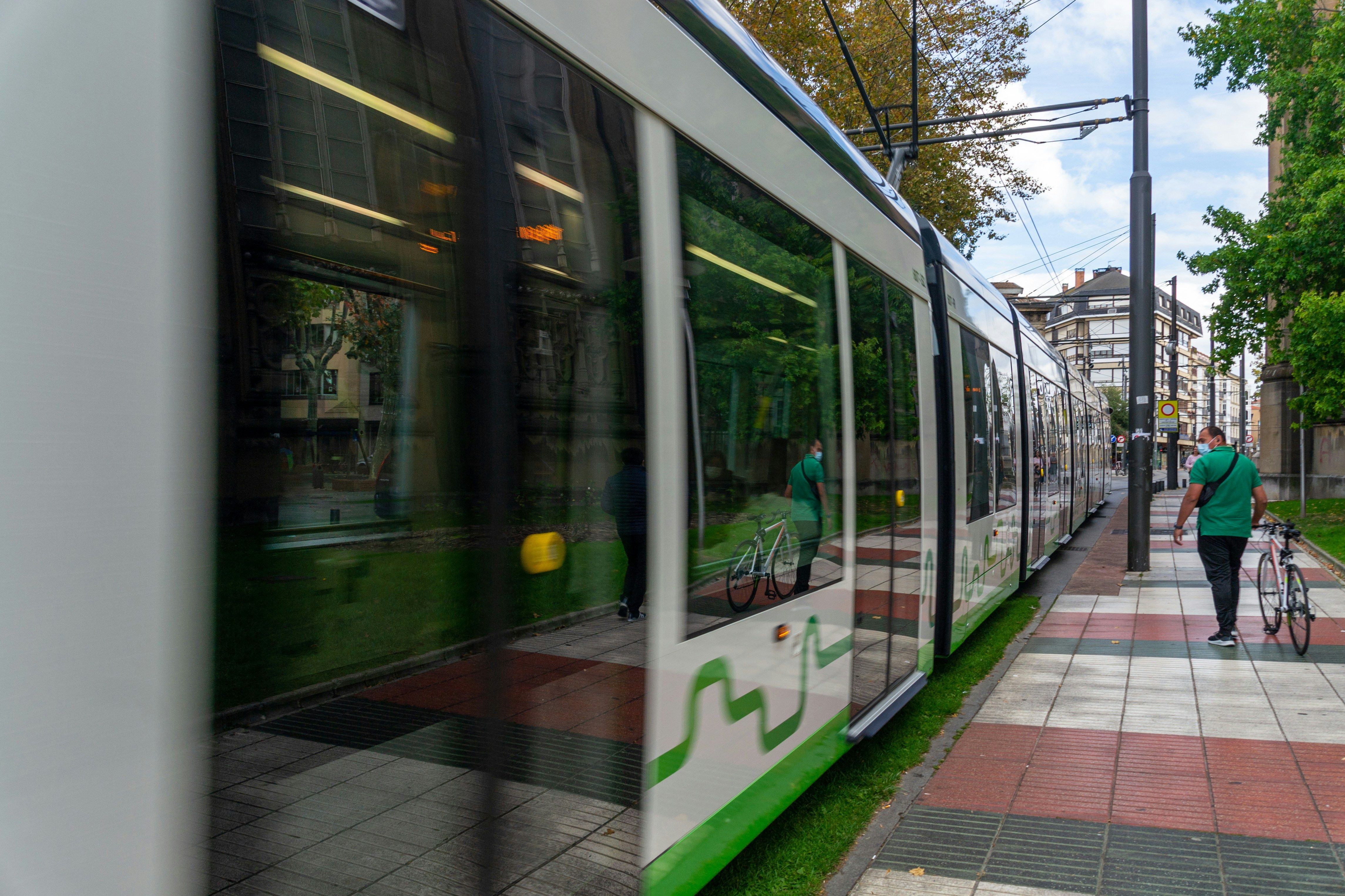 Main Image: Person walking down the street next to a green train portraying public transportation in Vitoria-Gasteiz, Spain