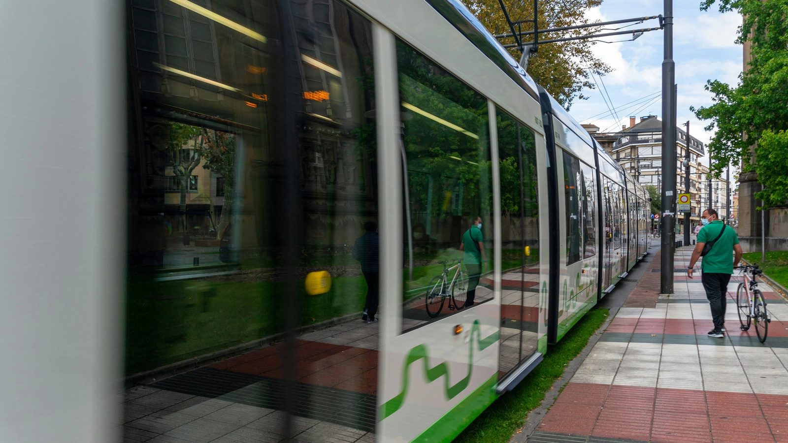 Main Image: Person walking down the street next to a green train portraying public transportation in Vitoria-Gasteiz, Spain