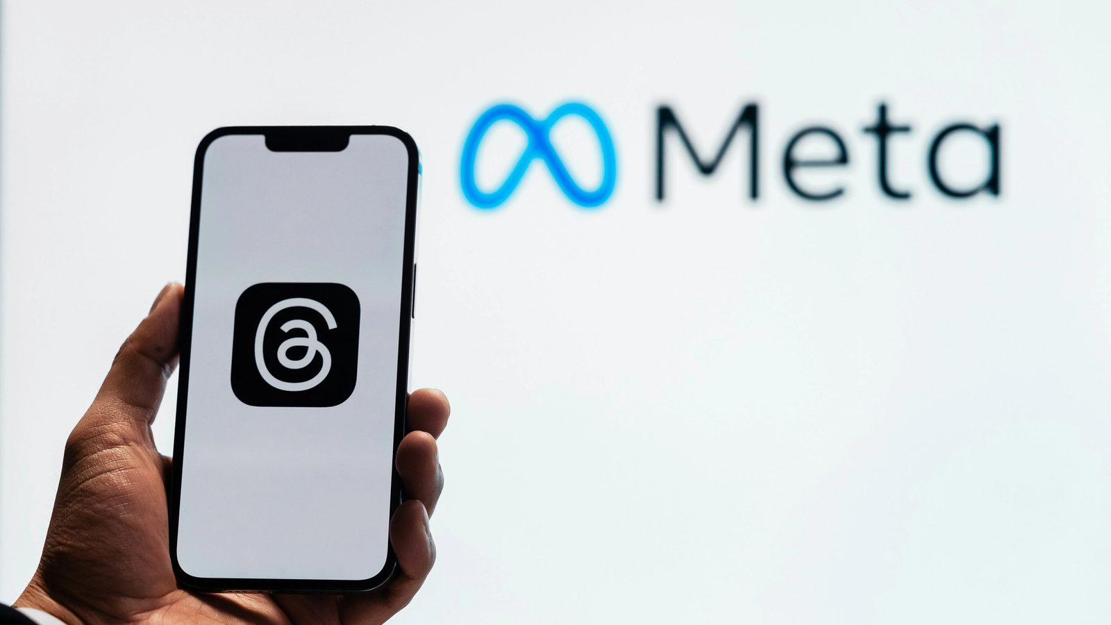 Main Image: Person using 'Threads' app with Meta logo on a wall in the background