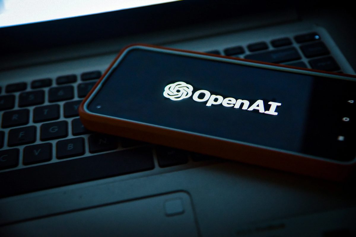 A cell phone sitting on top of a laptop computer with "Open AI" written on it.