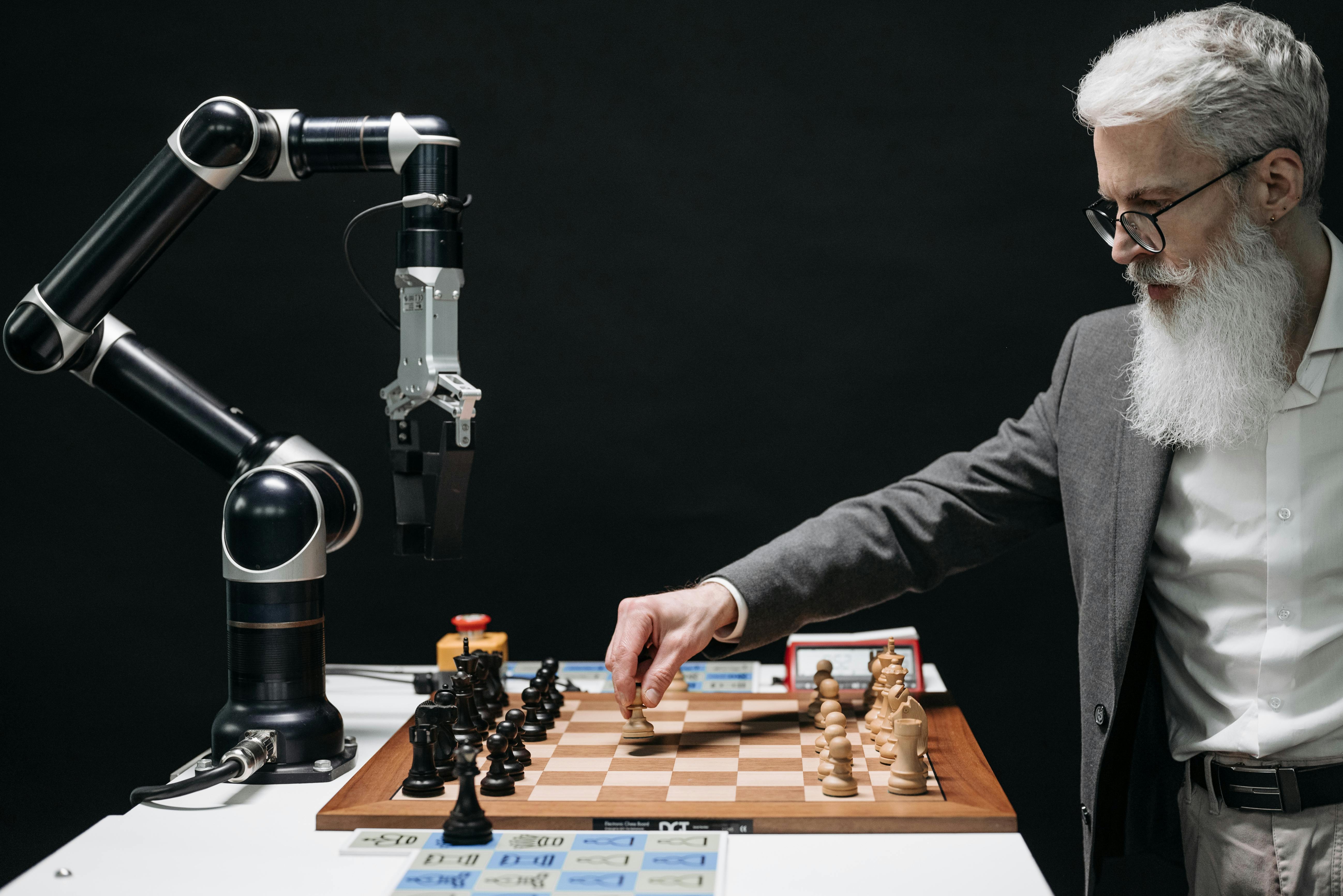 A bearded man playing chess against a robot