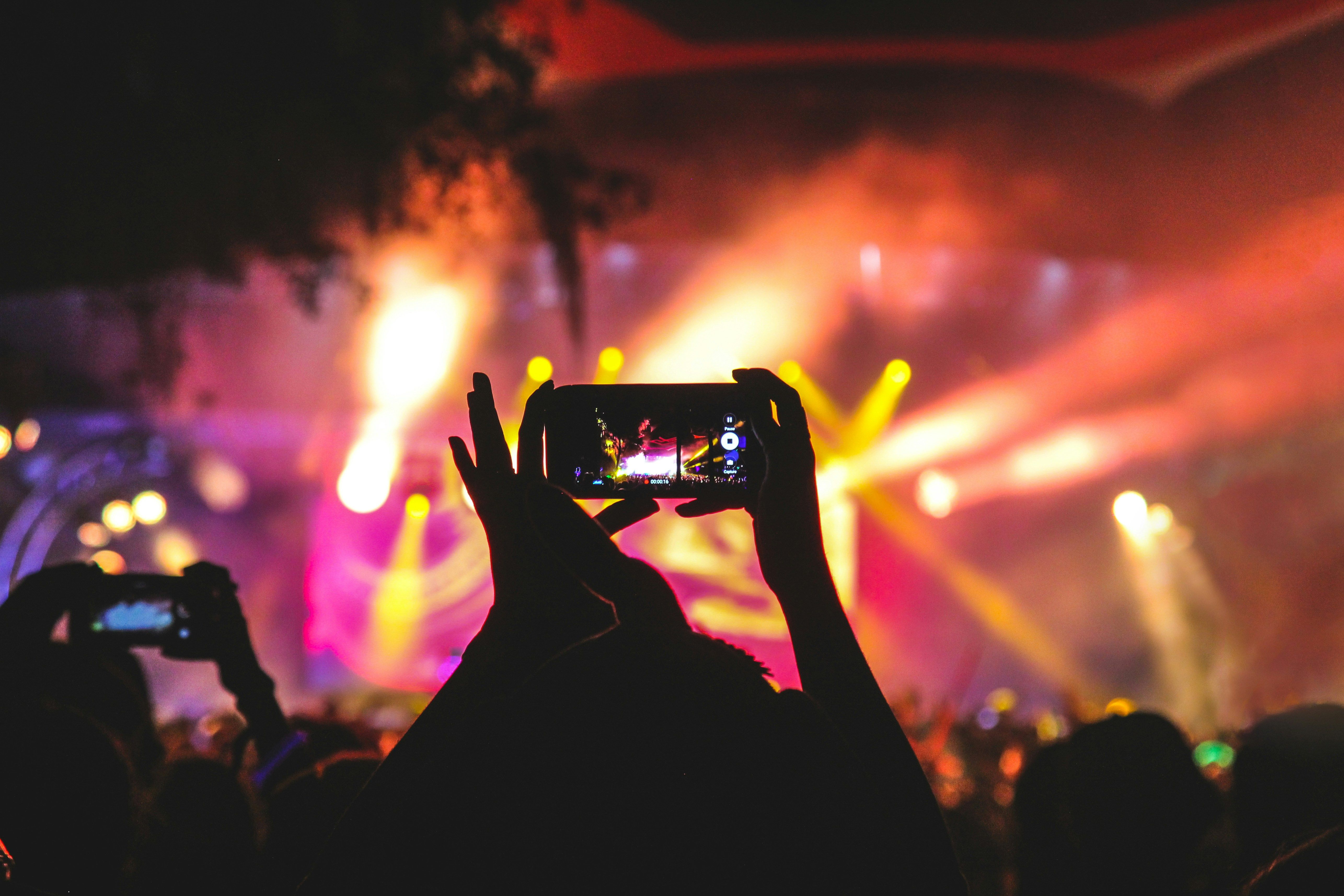 A person holding smartphone taking video of a concert near stage with lights during nighttime