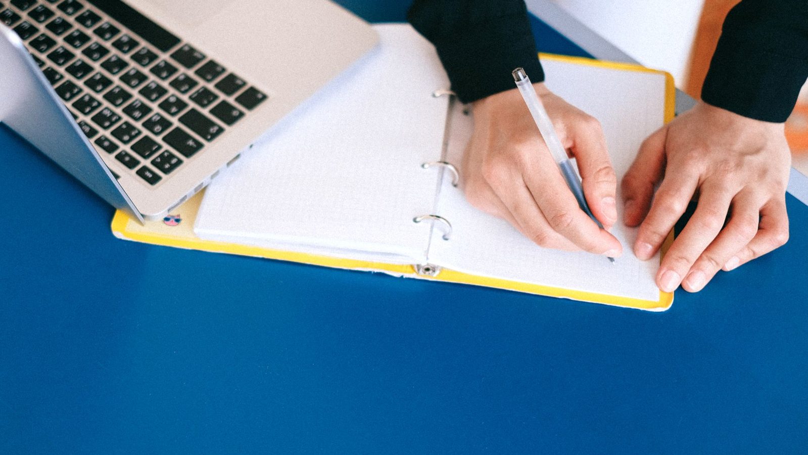 Taking notes on a laptop beside a notebook