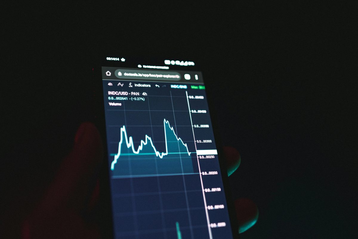 Person holding a mobile phone reading stock charts.