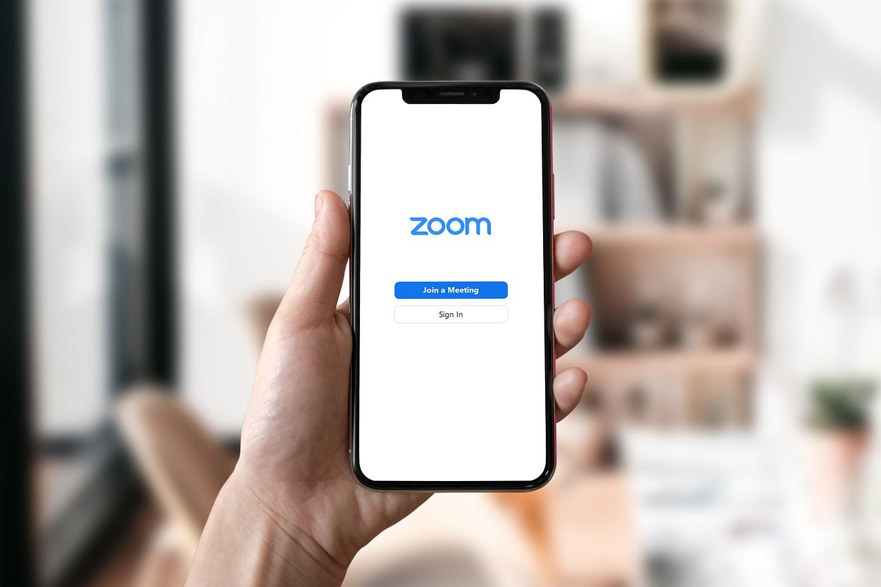 A person holding a phone up with Zoom app launched on the screen