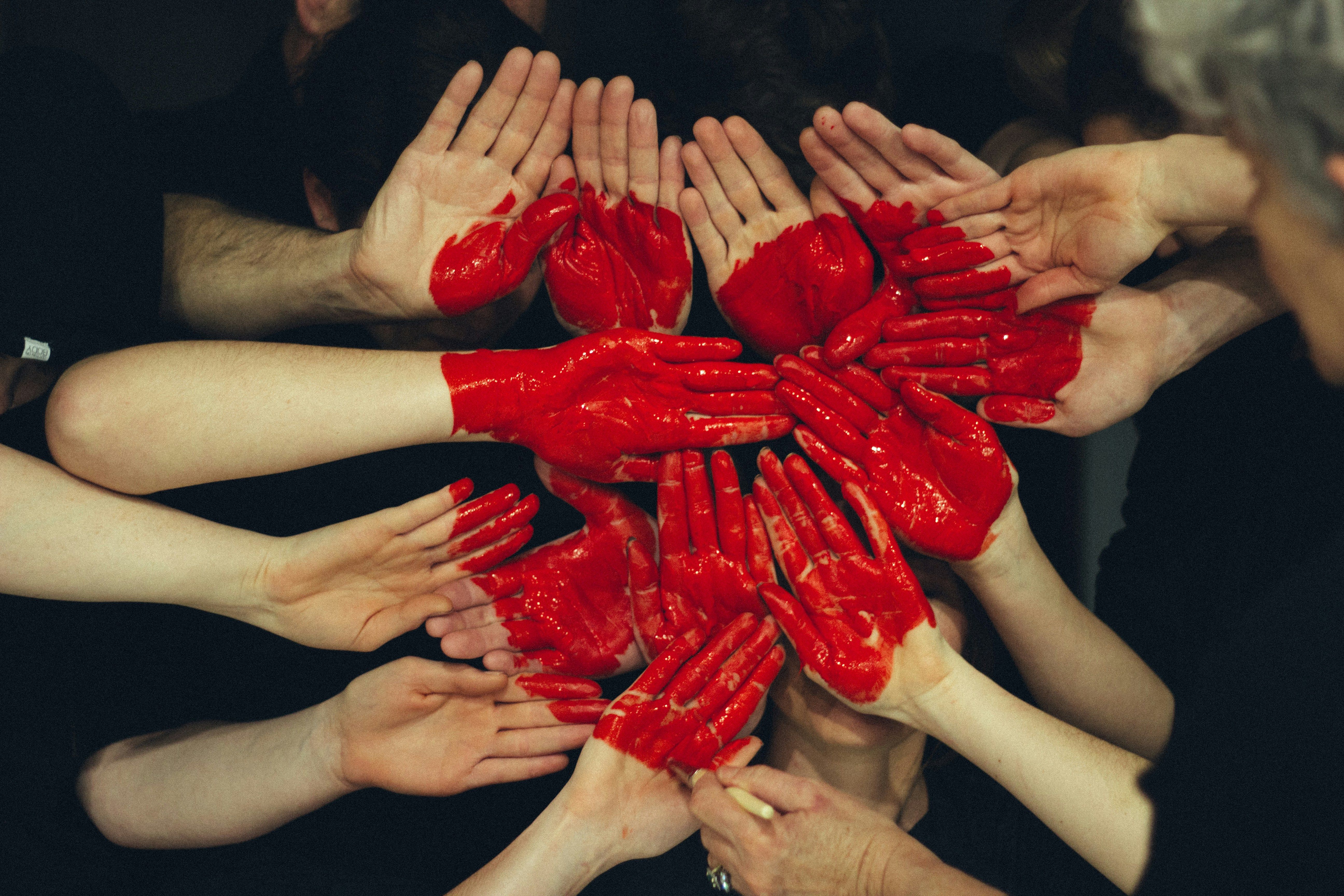 Several hands linked together and painted red to show a love symbol