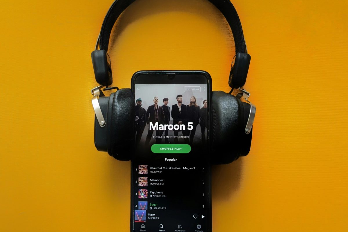 A phone with headphones on it playing a song on Spotify