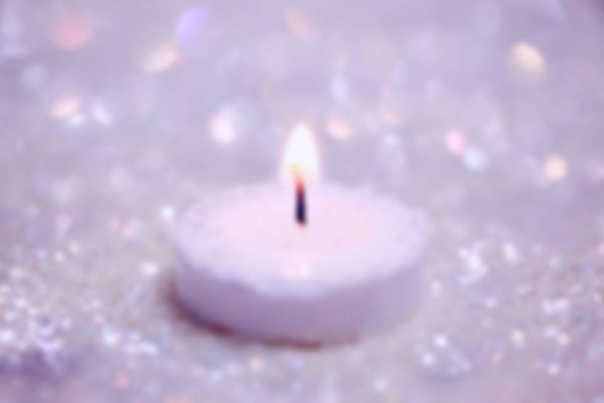 A single lit white candle surrounding by glitter