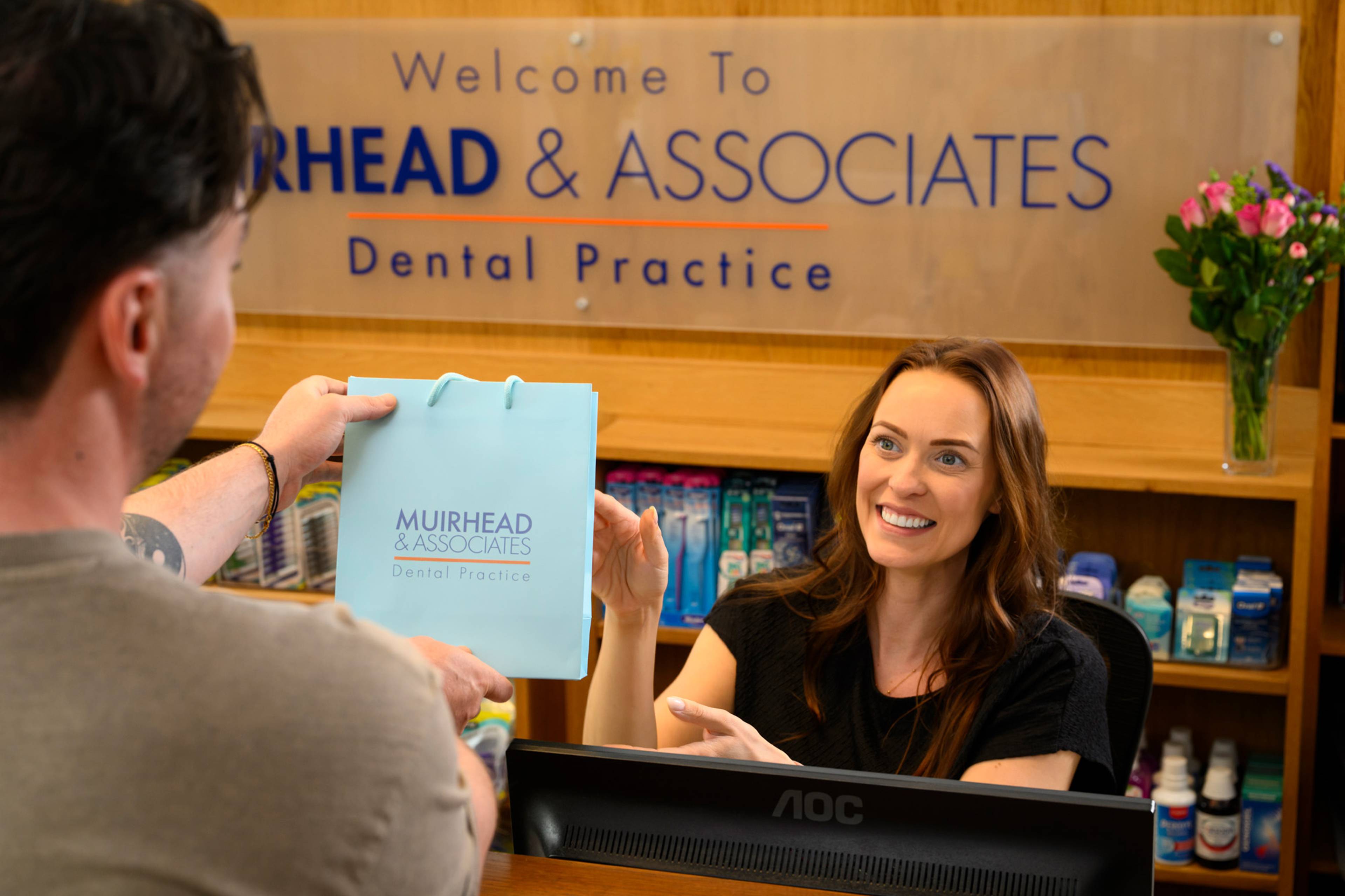 Practice Manager Rose Minney hands a branded paper bag to a patient