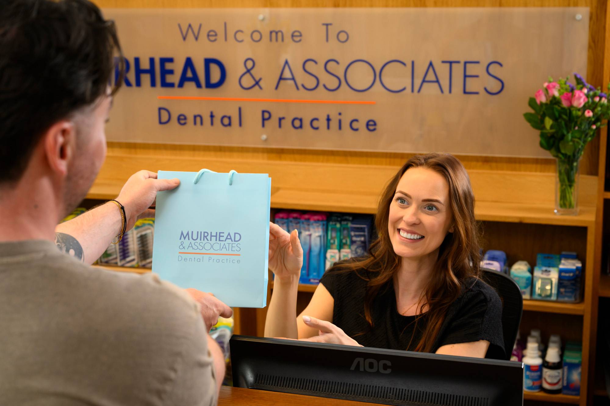 Practice Manager Rose Minney hands a branded paper bag to a patient