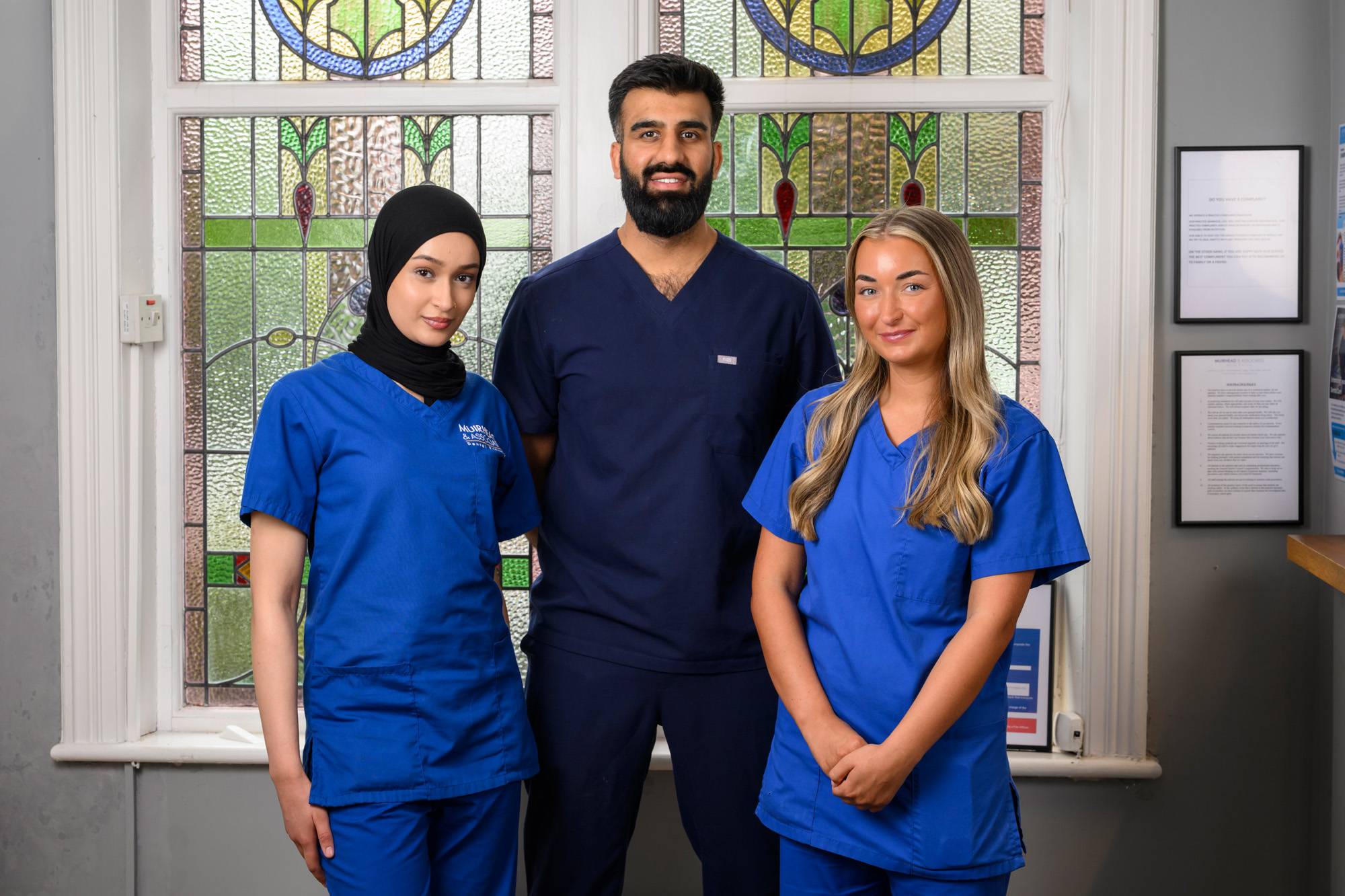 Ahmer, Shifah, and Angel in front of stained glass windows in our practice
