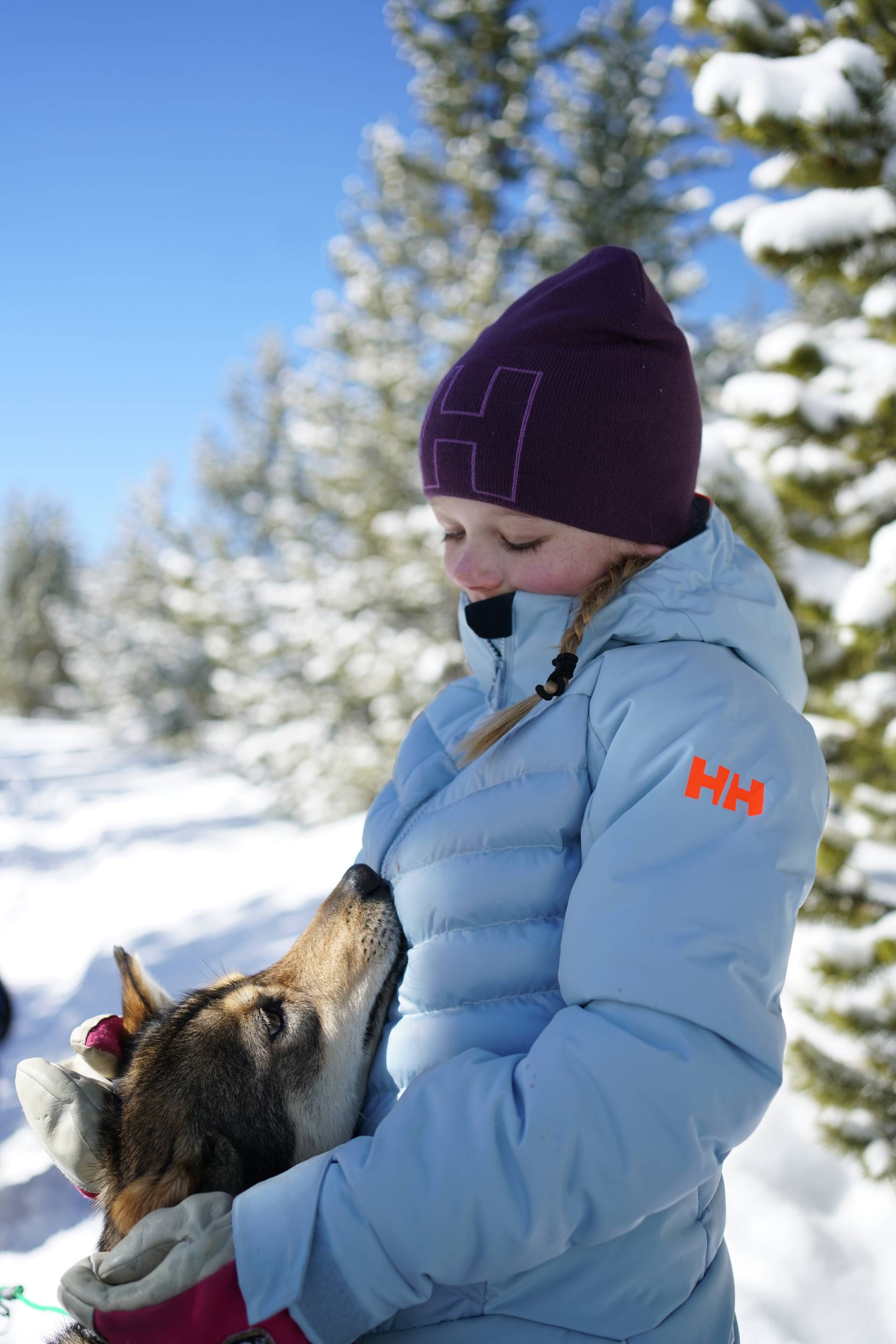 Girl in winter gear petting a sled dog