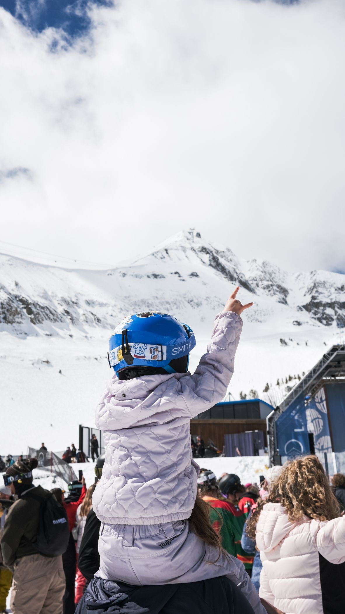 Girl in ski gear sitting on her parent's shoulders at a live music event