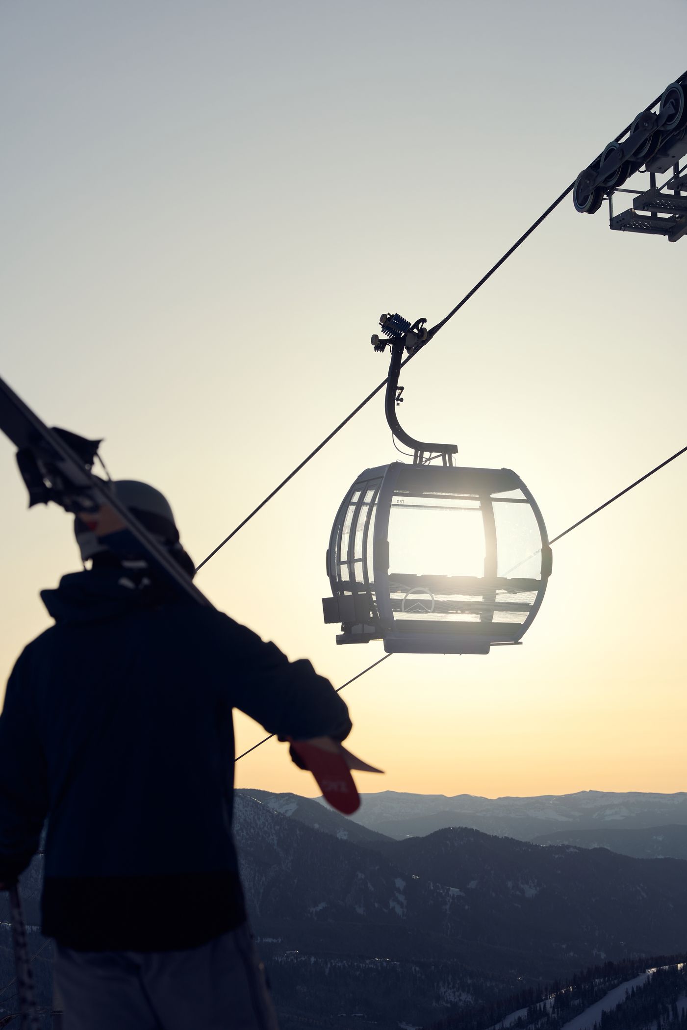 Person carrying their skis with an Explorer Gondola cabin in the background