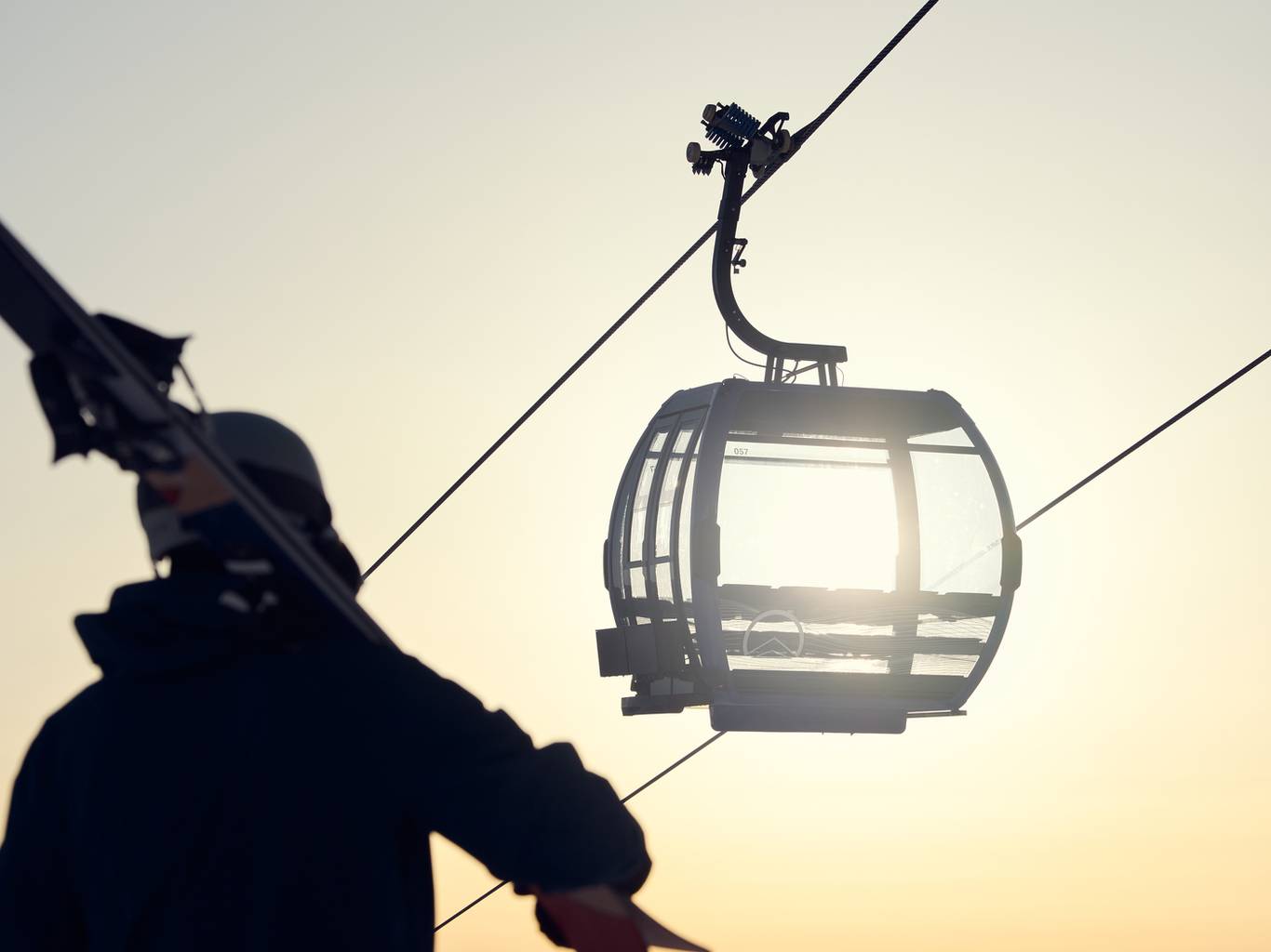 Person holding their skis with a gondola cabin in the background