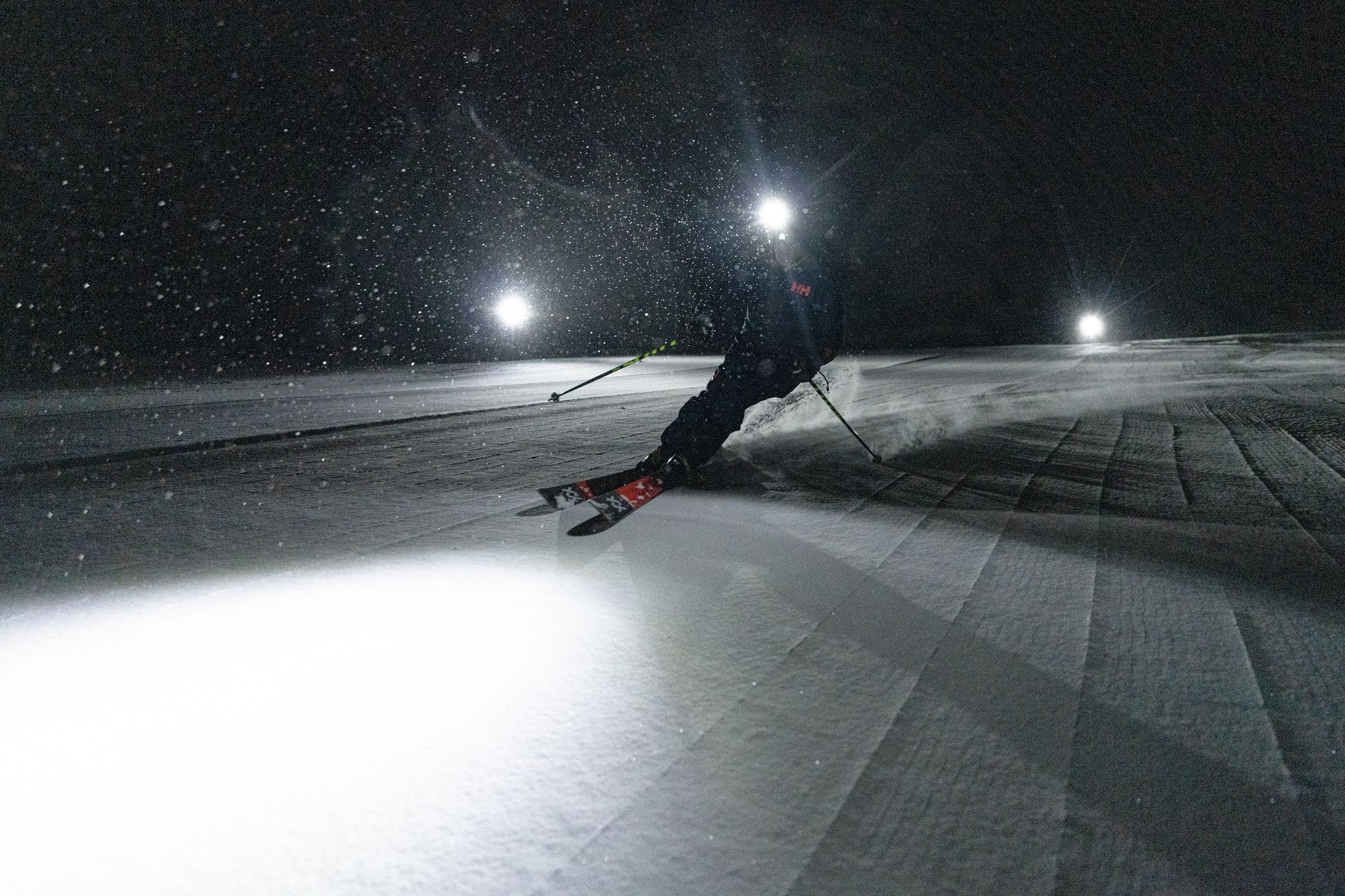 A skier on a groomed run at night illuminated by a headlamp