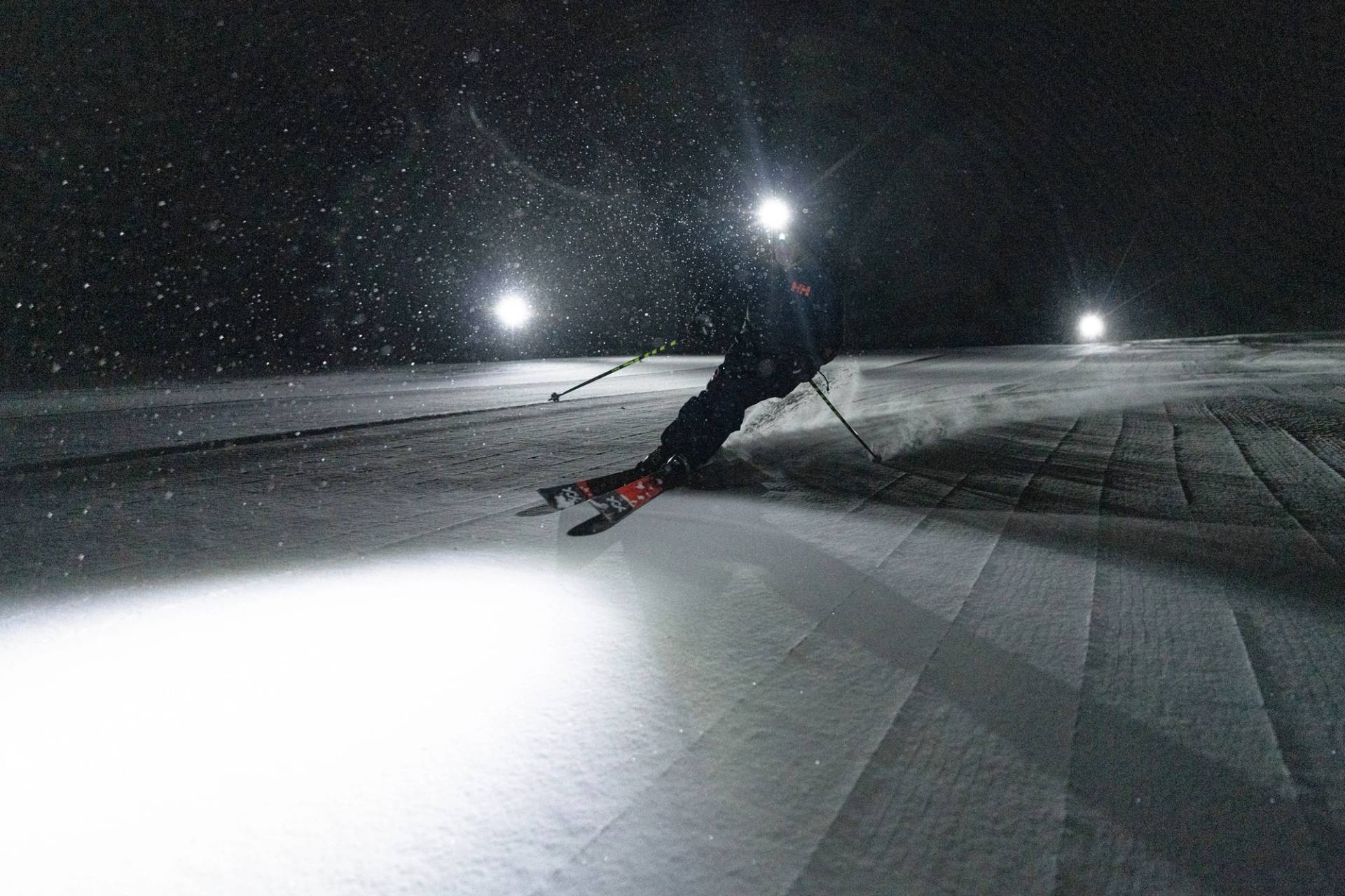 A skier on a groomed run at night illuminated by a headlamp