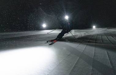A skier on a groomed run at night illuminated by a headlamp