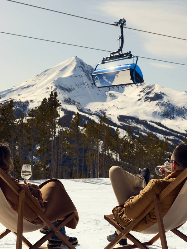 People sitting in lounge chairs with a chairlift and mountain peak in the background