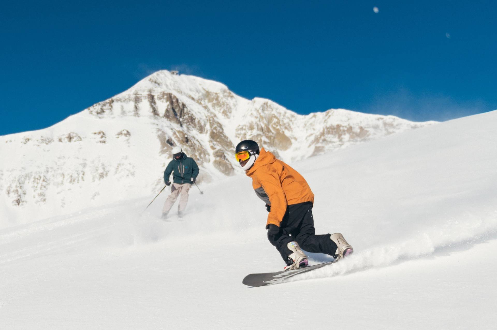 Skier and snowboarder on a groomed run with Lone Mountain in the background