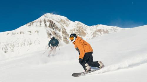 Skier and snowboarder on a groomed run with Lone Mountain in the background