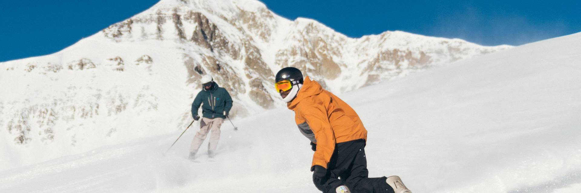 Skier and snowboarder in front of Lone Mountain