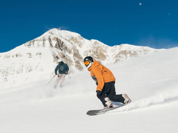 Skier and snowboarder in front of Lone Mountain