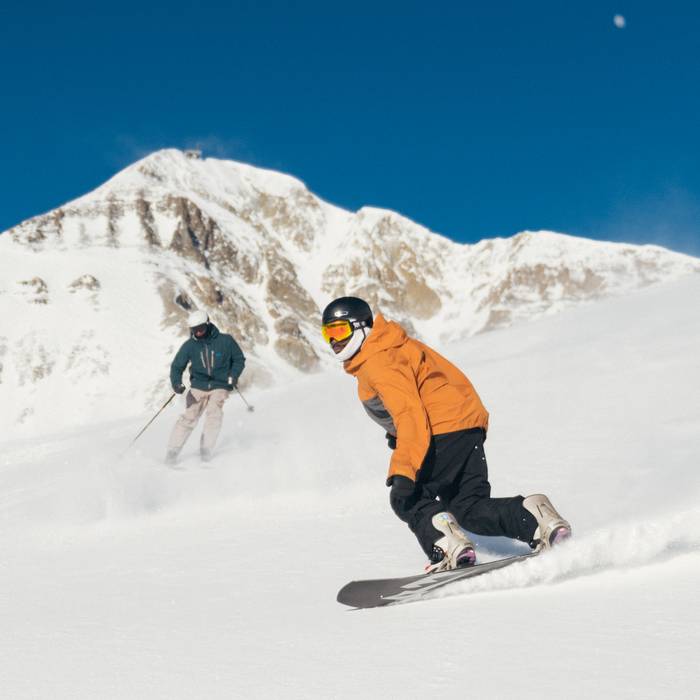 Skier and snowboarder on a groomed run with Lone Mountain in the background