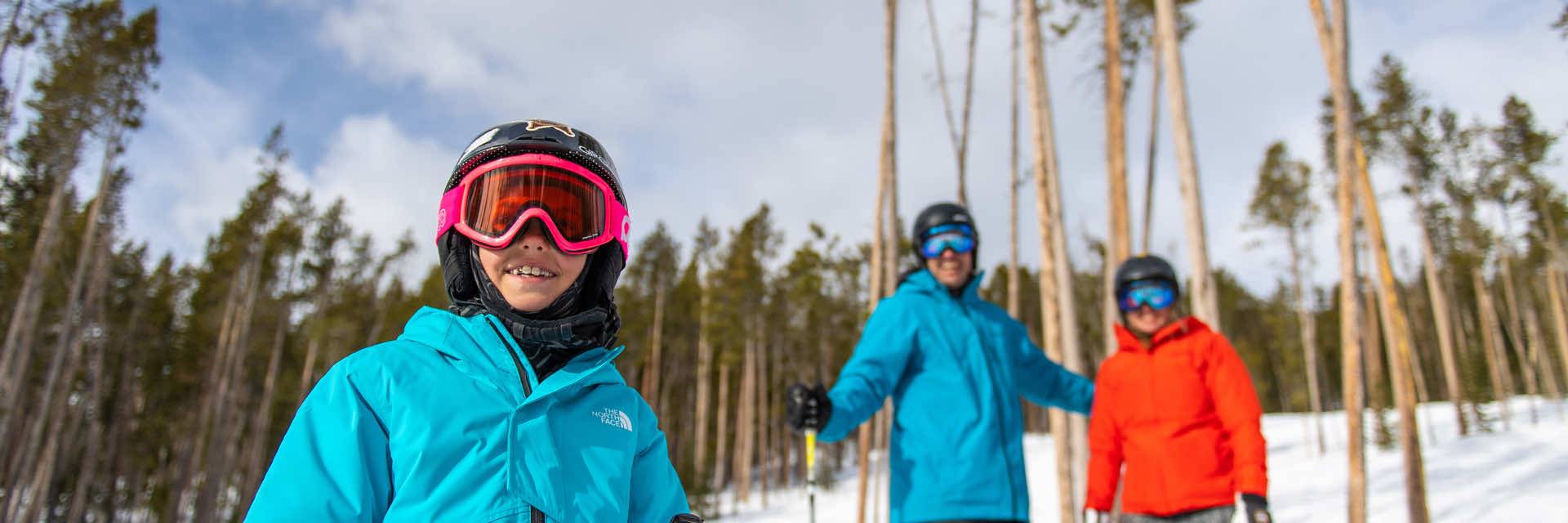 A child smiles in front of her parents while skiing in the trees