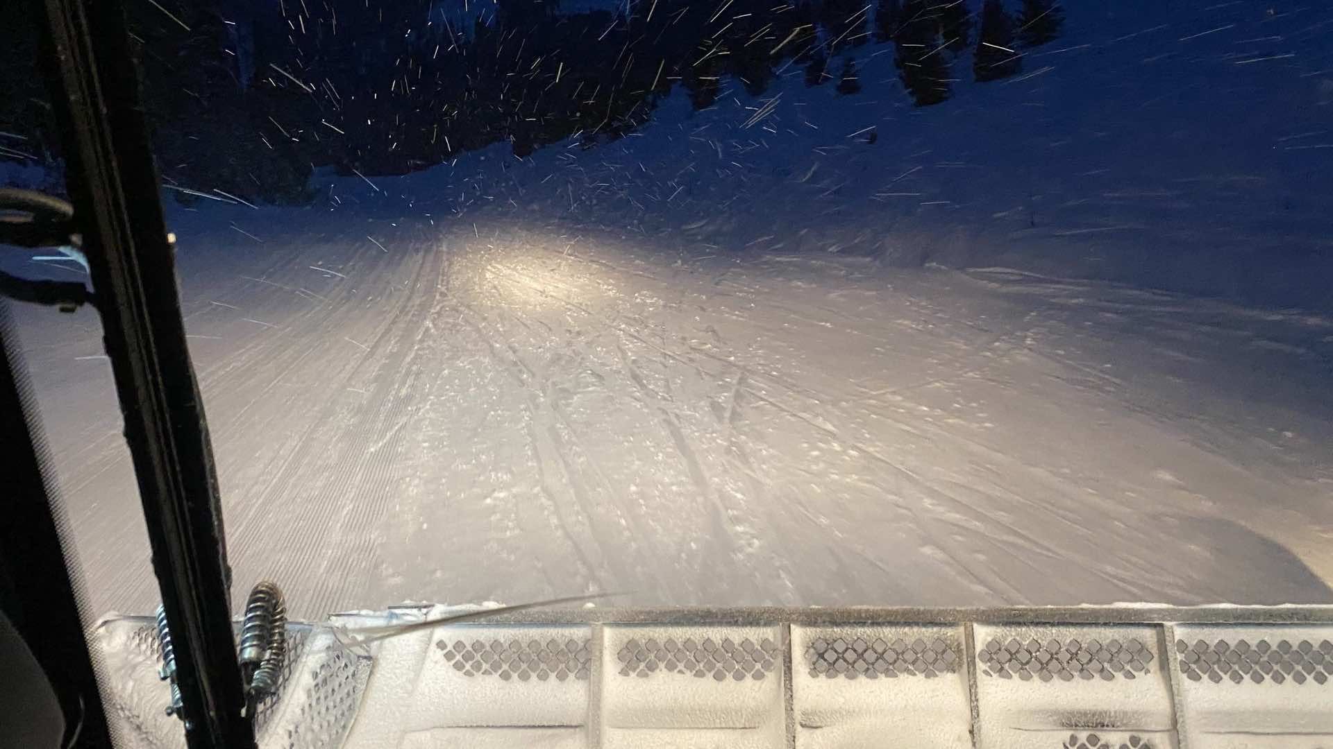 The headlights from the snowcat illuminate the way down the cat track