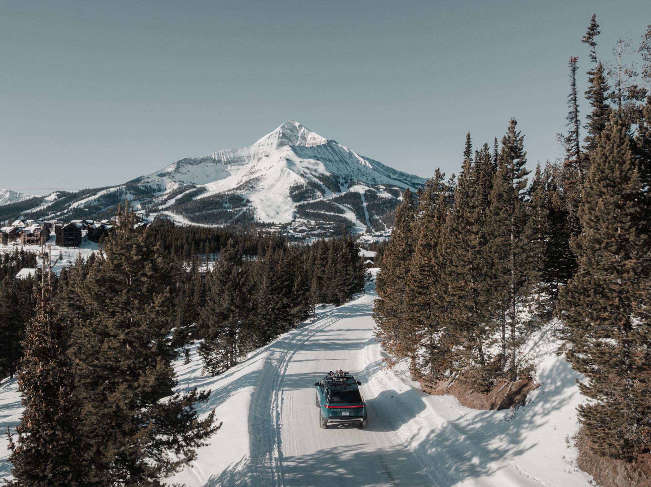 Rivian truck on a snowy road with Big Sky Resort in the background