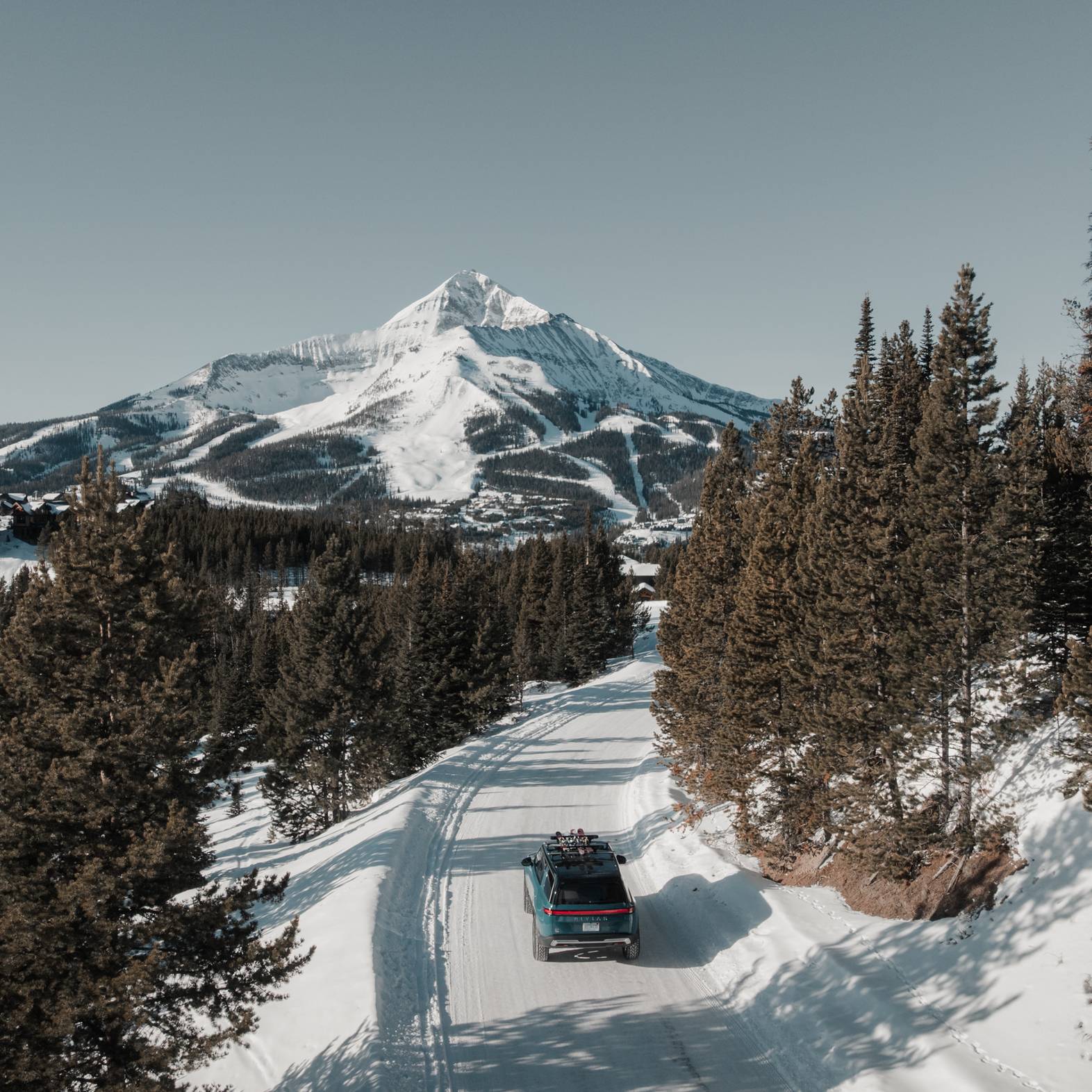 Rivian truck on a snowy road with Big Sky Resort in the background