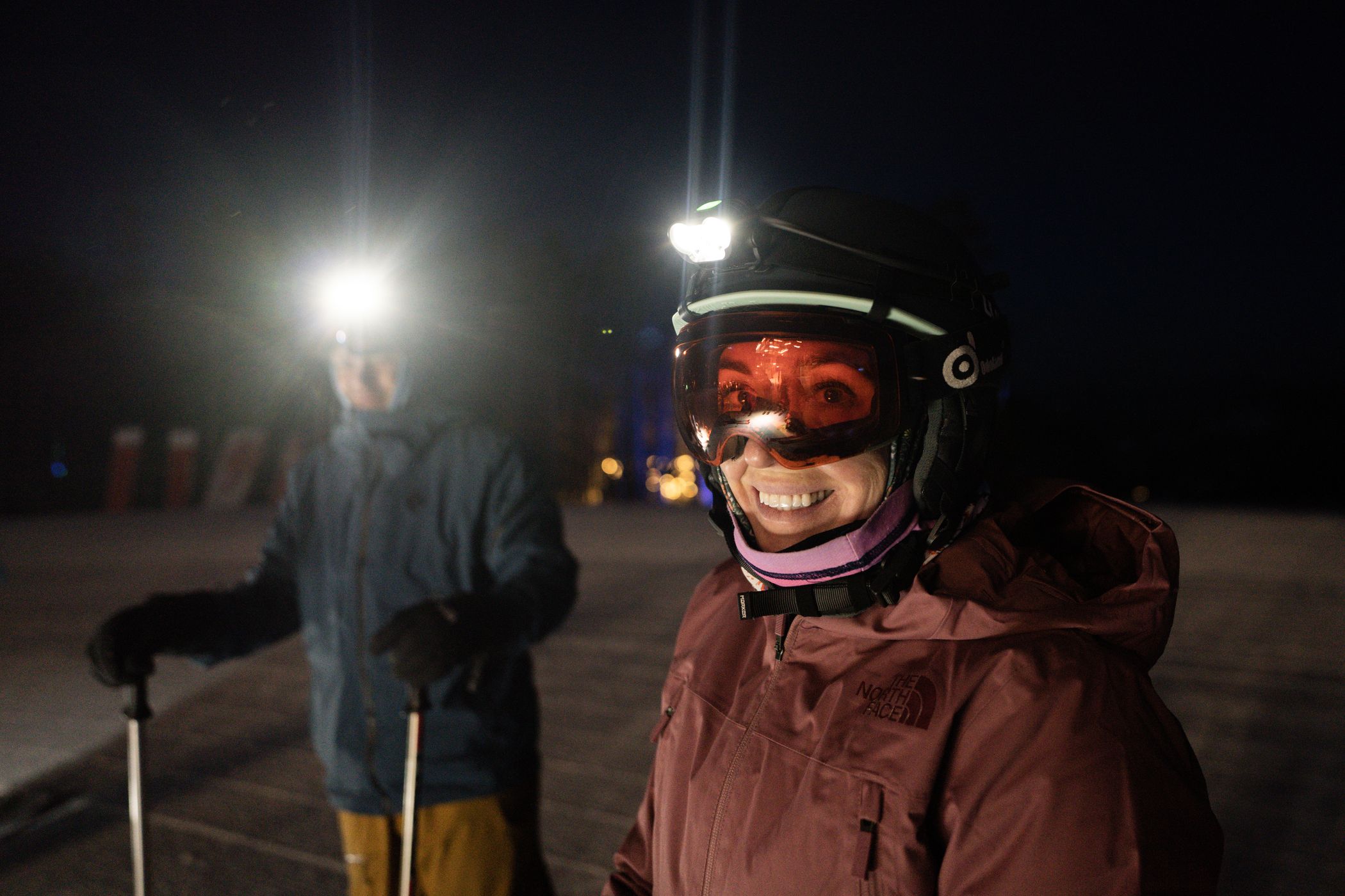 Two people in ski gear with headlamps at night